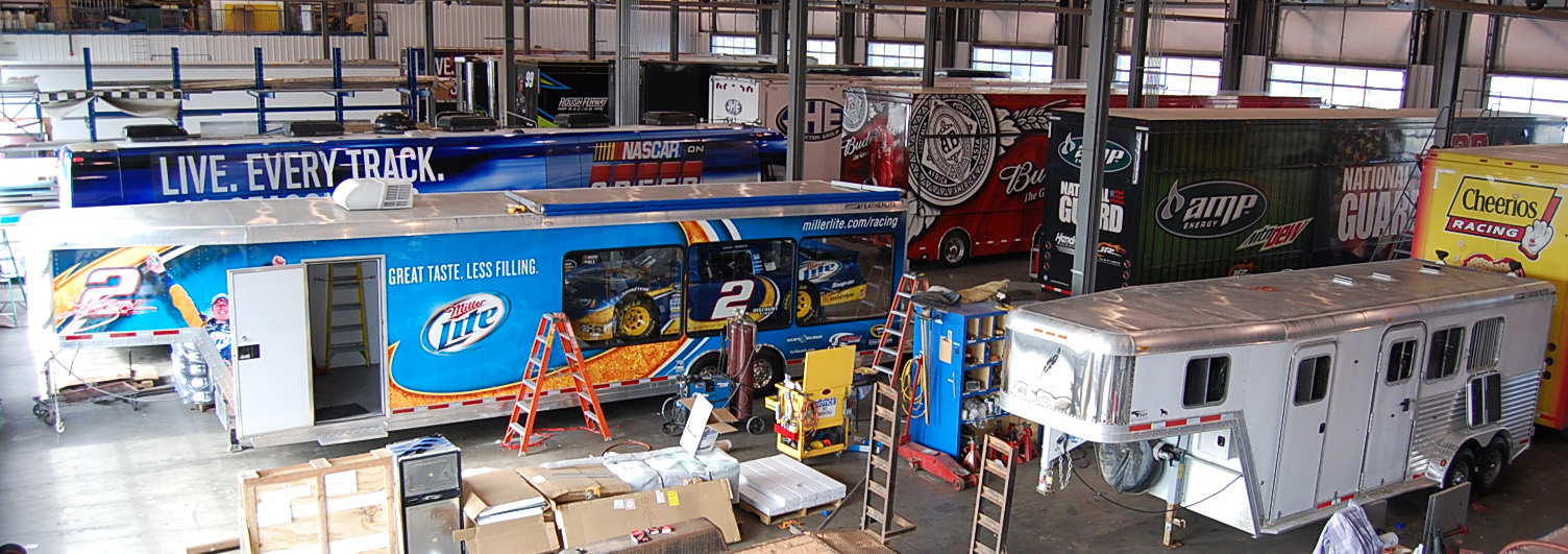 A Miller Lite sponsored trailer carrying a racecar in a giant service warehouse with other Nascar equipment